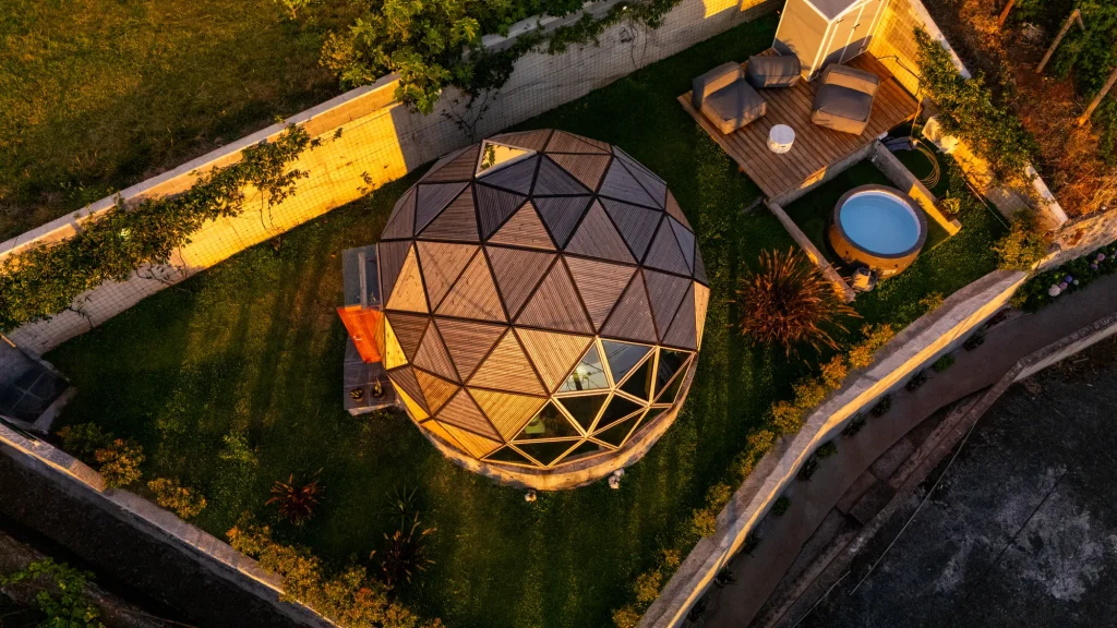 Le dôme géodésique et le jardin de la Villa Domaterra I à la tombée du jour, avec sa terrasse en bois, ses assises de détente et son jacuzzi rond