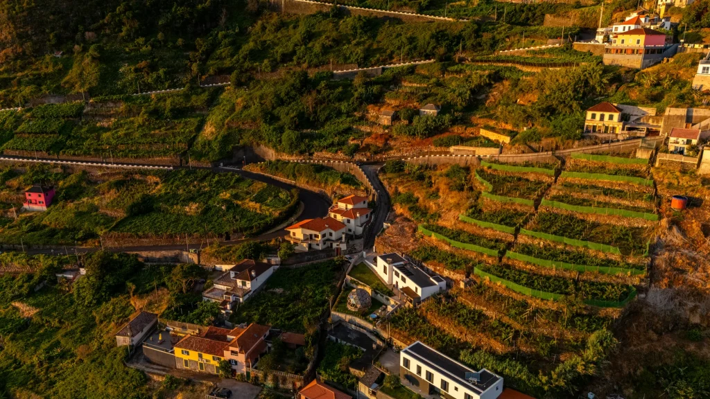 Vue aérienne de la route sinueuse et du coteau de vignes en terrasses au-dessus de Porto Moniz, le dôme de la Villa Domaterra I visible parmi les maisons