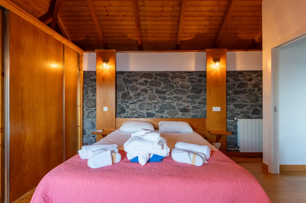 Um quarto da Villa Escaleiras com uma parede de destaque em pedra vulcânica e colcha cor-de-rosa
