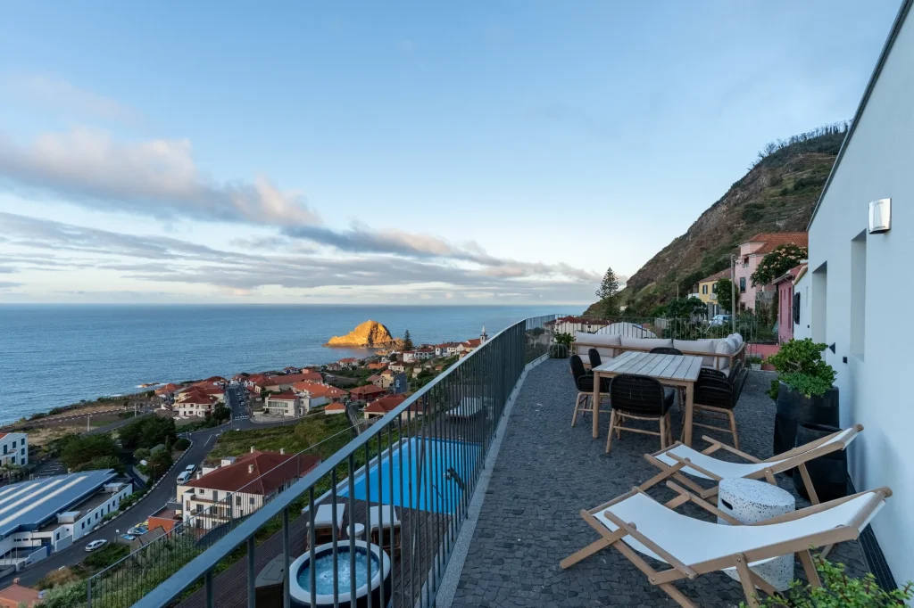 O terraço da Villa Escaleiras ao anoitecer, com mesa de jantar e espreguiçadeiras sobre o Porto Moniz