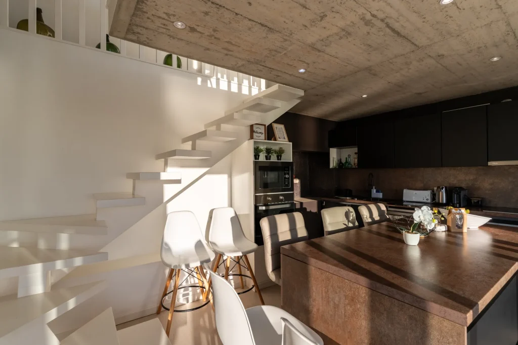 Villa Espigão's open-plan kitchen and dining island beneath the mezzanine, with a floating staircase