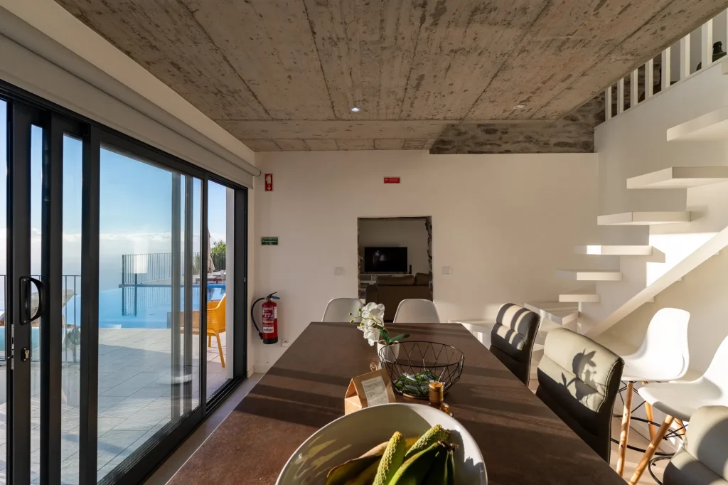 Villa Espigão's dining table with the infinity pool and Atlantic view through the sliding doors, staircase behind