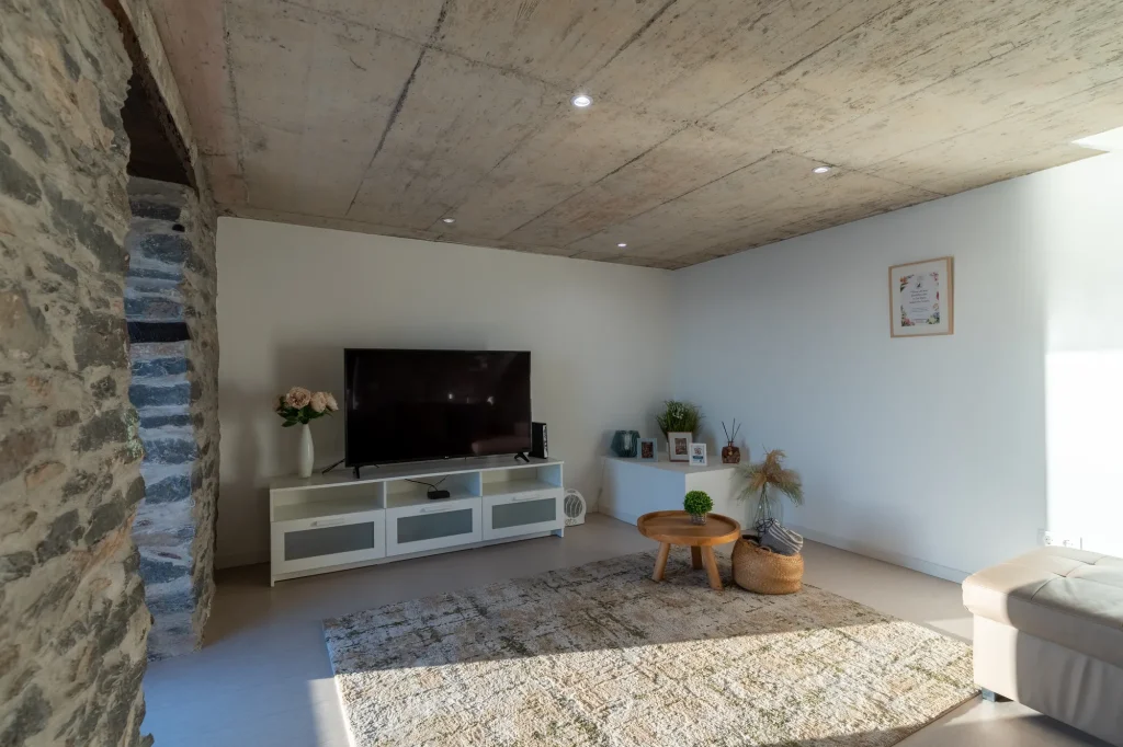Villa Espigão's living room with a wall-mounted TV against exposed stone, floating staircase alongside