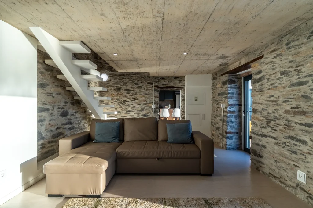 Villa Espigão's living room with a stone chimney breast and floating staircase up to the mezzanine