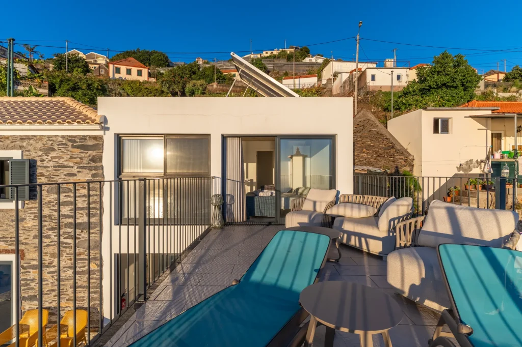 Villa Espigão's terrace at dusk, lounge seating beside the sliding doors, hillside village behind