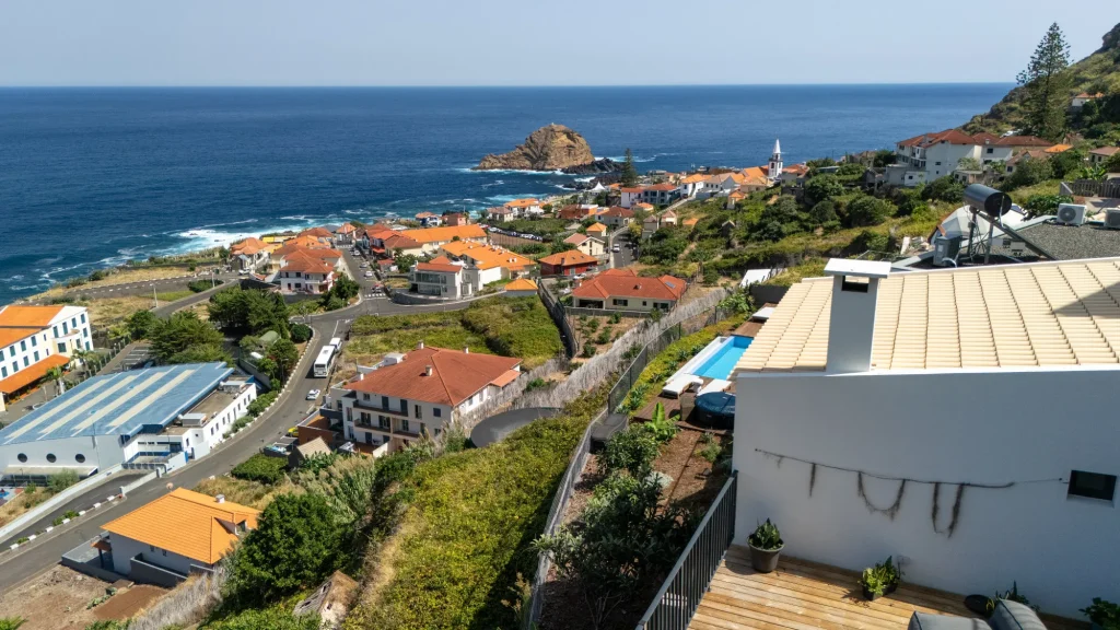 Porto Moniz and its islet seen from the hillside at Villa Domaterra II, a white house with a pool terrace in the foreground