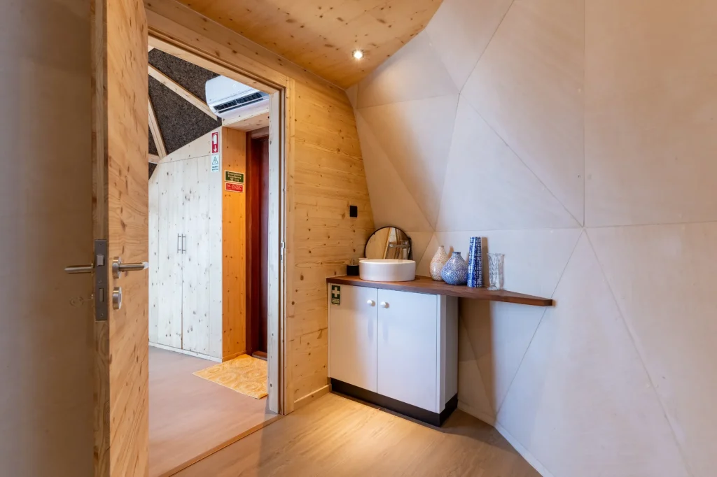 Villa Domaterra II's vanity, a vessel sink on a white cabinet against the dome's pale panelled wall, the bedroom through the open door