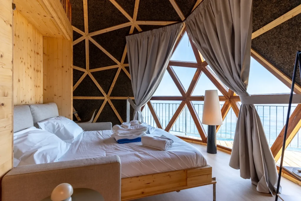 Villa Domaterra II's bedroom, the bed facing the dome's triangular windows and the Atlantic, curtains tied back