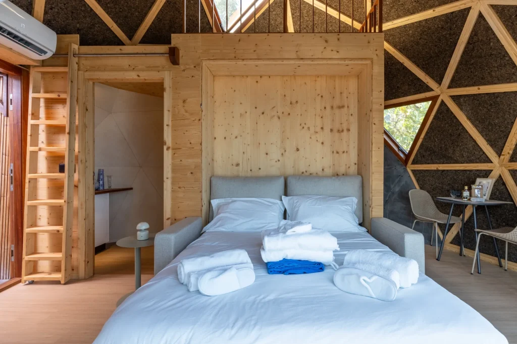 Villa Domaterra II's bed set with towels and slippers before a pine wall, a ladder up to the mezzanine at its side