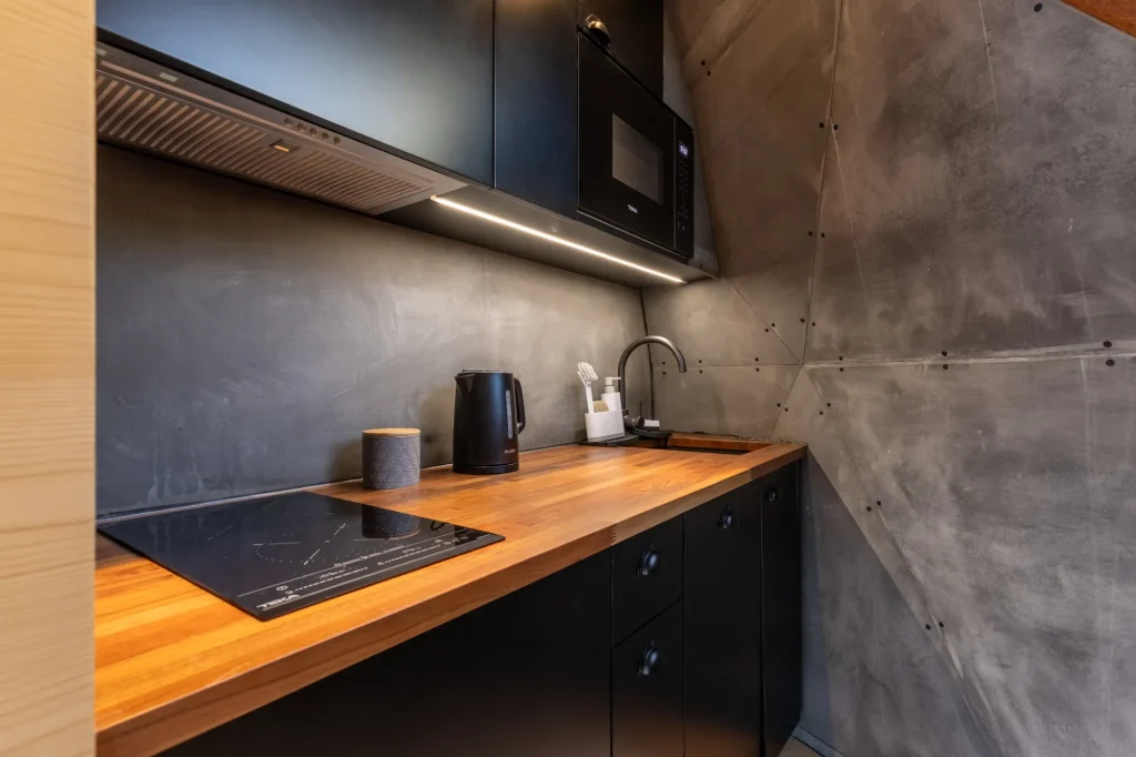 Villa Domaterra II's kitchenette, a wooden worktop with induction hob, kettle and sink beneath black cabinets and a microwave