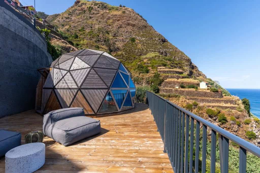 Villa Domaterra II's geodesic dome on its wooden deck, with lounge seating beneath a terraced hillside and the sea beyond