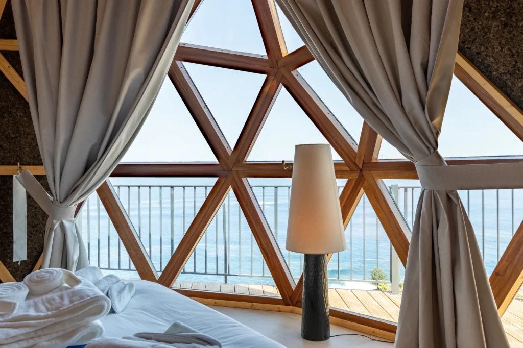 The Atlantic through Villa Domaterra II's triangular dome windows, framed by tied-back curtains and a floor lamp